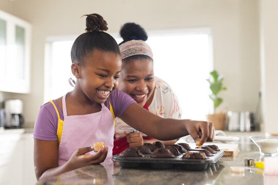 Happy african american mother and daughter decorating cupcakes in kitchen