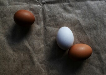 Close-up image of three eggs resting on a piece of paper, one of them is white