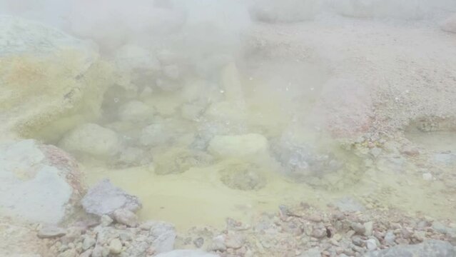 Steam drifting over a pool of boiling hot bubbling water containing sulphur in a volcano crater