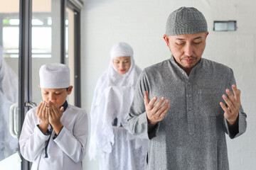 Asian muslim family, father, mother and son praying dua together at mosque. Raising hands pray dua