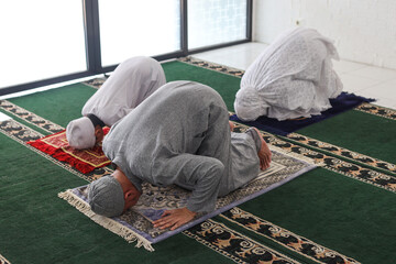 Asian muslim family praying jamaah together and doing sujud movement or called a Sajdah or...