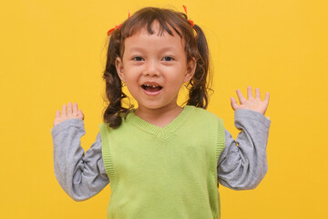 Young excited surprise smiling little girl child raised hands isolated on yellow color background
