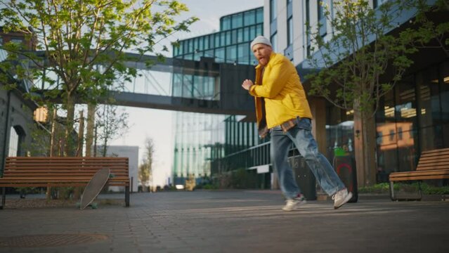 Young And Athletic B-Boy Breakdancing To Break Beats On The City Street Among Modern Buildings Alone With A Speaker. Fashionable Man Practicing Freestyle Choreography For Upcoming Break Dance Battle.