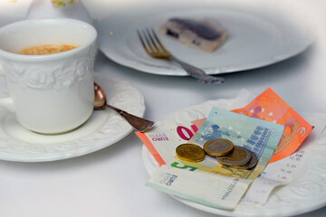 top view close-up on white plate with euro bills and coins, selective focus, cup of coffee, dishes with food, lunch concept in restaurant, cafe, tip money concept, change of waiter