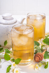 Organic herbal health summer cold drink. Jasmine flowers green tea, in glass, with ice cubes, teapot, on white table, with blooming jasmine flowers 