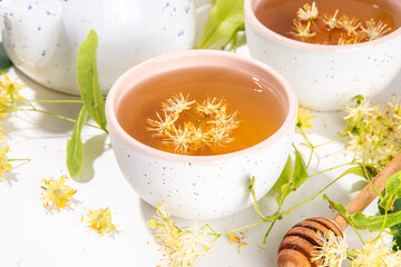 Organic herbal health drink. Linden plant flower green tea, in white mugs, with a teapot, on a white table, with copy space and blooming linden inflorescences and flowers