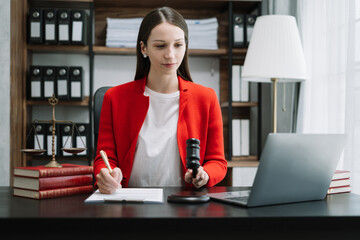 Justice and law concept. Female judge in a courtroom the gavel, working with digital tablet computer on wood table in sun light.