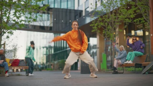Point Tracking Edit Of Young Stylish Female Hip-Hop Dancer Freestyling On City Street Among Modern Buildings. Friends Relaxing On Background, Supporting Street Style Performer Practising Choreography.
