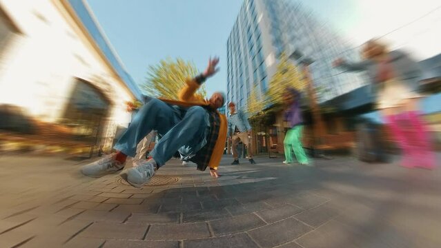 Trendy Zoom Blur Edit of Young Stylish B-boy Breakdancing On City Street Among Modern Buildings In Urban Area. Group Of Friends Cheering On Background, Supporting Breakdancer Practising Choreography.