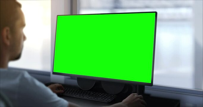 An engineer works on a computer with a green screen. In the background, there is a production hall, a template for work in a design facility in the technological, mechanical, or IT industry