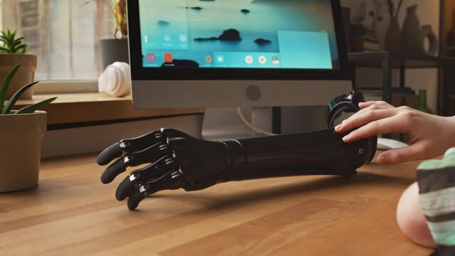 Cropped shot of unrecognizable woman touching her arm prosthesis on wooden table gently with fingers