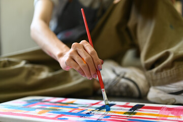 Naklejka premium Image of male artist sitting on floor in art studio and painting on canvas with watercolors. Creative hobby and art concept