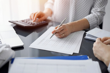 Woman accountant using a calculator and laptop computer while counting taxes for a client. Business audit and finance concepts
