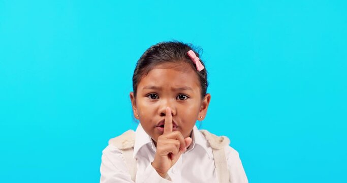 Finger on lips, silent and secret with a girl on a blue background in studio for gossip or news. Portrait, whisper and quiet with a cute or sneaky female child posing to hear private information