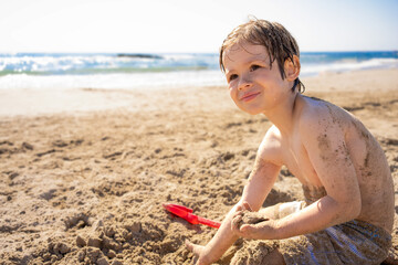Close portrait of little blond child boy stand posing on the beach over sky with waves