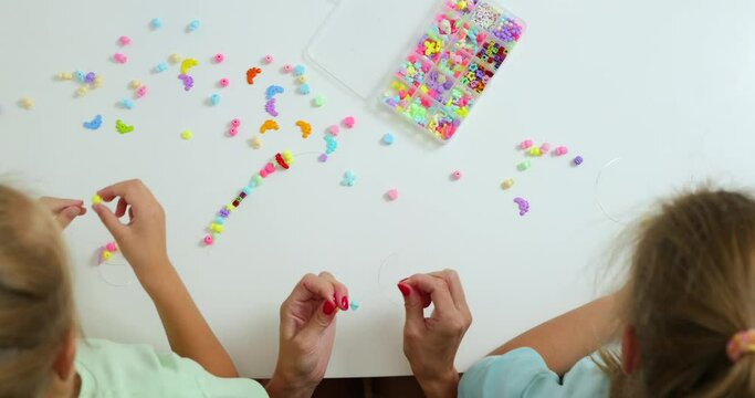 Happy mother with her daughters making beaded jewelry at home