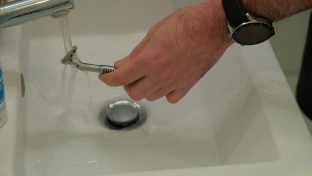 Cleaning shaving razor in bathroom sink. Rinsing off razor with water.