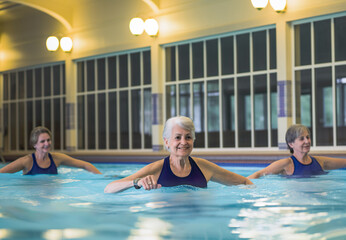 Fototapeta premium Enthusiastic senior women doing aqua aerobics in an indoor swimming pool, AI generated