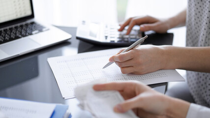 Woman accountant using a calculator and laptop computer while counting taxes with a client or colleague. Business audit team