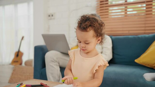 Modern parents working by computer and tablet while cute little daughter drawing a picture in living room at home. Happy father mother and daughter to spend time together at home. Family concept