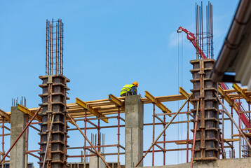 A male construction worker stands on reinforced concrete beams at a height.