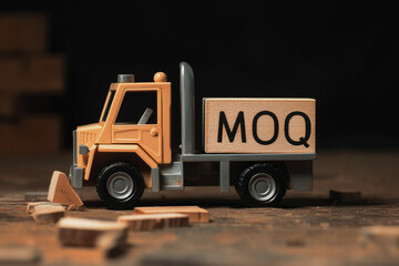Toy yellow truck with wooden block with letters MOQ engraved: Abbreviation of Minimum Order Quantity, warehouse dark background