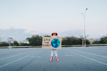 Girl dressed as astronaut showing Save The Planet cut out standing in parking lot
