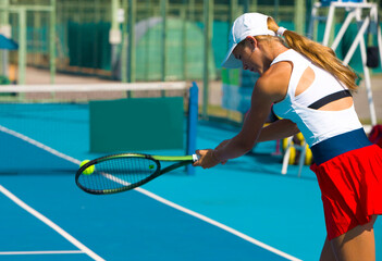 A girl plays tennis on a court on a summer sunny day