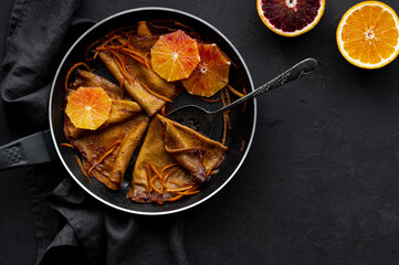 Traditional French Crêpes suzette pancakes with orange sauce in a pan on a black stone background...
