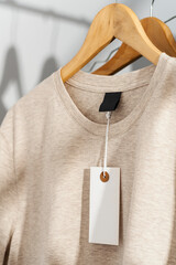 Beige t-shirt with blank price tag on wooden hanger