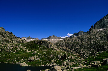 A high mountain landscape in Spain: green meadows, rocky peaks, and a tranquil pond.