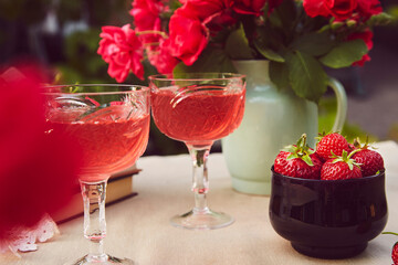 Cozy aesthetic table setting. Couple of glasess with red homemade, strawberry infusion, wine. Roses bouquet