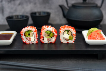 Sushi with red caviar near Japanese cast iron tea pot and cups, with chopsticks, on a black background. Japanese cuisine