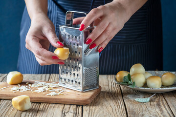 A woman is grating smoked mozzarella balls on stainless grater, cutting board, sage leaves over wooden table
