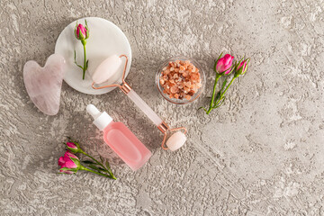 A set of cosmetics and a rose quartz roller for home care. Spa and relaxation concept. Gray cement background. Top view.