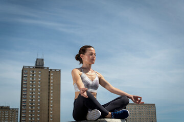 Mid adult woman practicing yoga and meditating, urban backdrop.