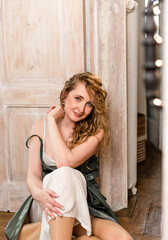 Plakat Young attractive girl with loose blonde curly hair in dress sitting on parquet floor