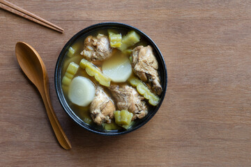 top view of chicken soup with chinese bitter gourd in a ceramic bowl on wooden table. asian homemade style food concept.
