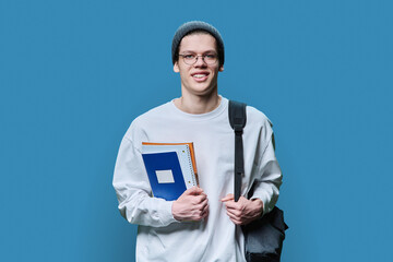 Young guy college student with backpack notebooks textbooks on blue background