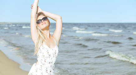 Fototapeta na wymiar Happy blonde woman in free happiness bliss on ocean beach standing with sun glasses