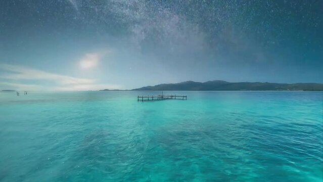 Footage of a stunning tropical island sea with clear, turquoise waters, showcasing the beauty of nature for a relaxing vacation, under a starlit sky revealing the breathtaking Milky Way