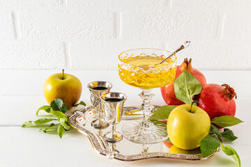 Beautiful still life with ripe pomegranates and apples, a silver glass of wine and a bowl of honey. White background. The concept of Rosh Hashanah.