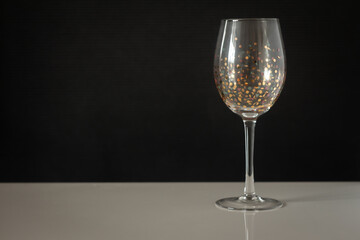 wine glass decorated with round sequins on a black background and a white table