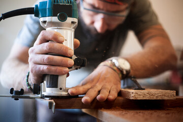 Close-up of a carpenter's hands using a router for woodworking. Selective focus.