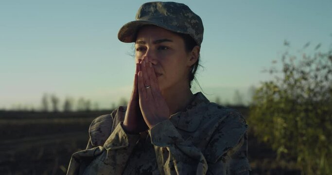 Cinematic Close Up Portrait of Young Female Patriotic Soldier Praying with Hope While Standing in a Field During Sunset. Emotional Woman in Camouflage Military Uniform Hoping for Peace and Freedom  