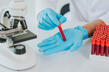 Close up of male doctor taking blood sample tube from rack with analyzer in lab / Technician holding blood test tube in research lab