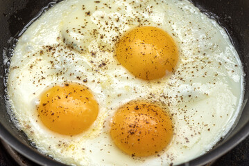 Fried eggs from three eggs sprinkled with pepper in a frying pan.
