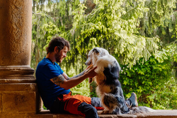 young Caucasian man enjoys playing with his border collie dog sitting in an old building. Practicing obedience with his dog.