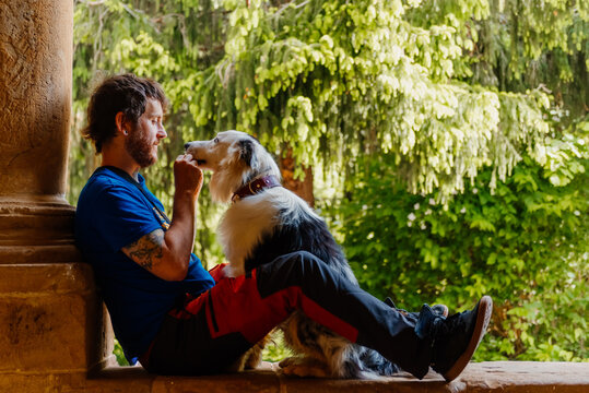 young Caucasian man enjoys playing with his border collie dog sitting in an old building. Practicing obedience with his dog.