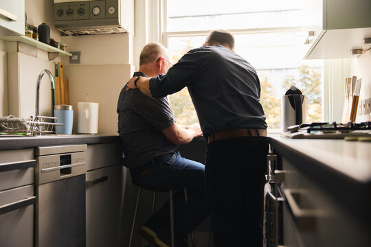 Same Sex Male Couple Working From Home In Kitchen Apartment